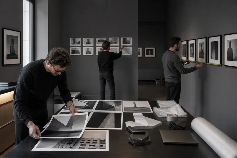Три участника проверяют фотографии и схему размещения в графитовом зале; иллюстрация к инструкции по планированию выставки в AI-GROK.CHAT.